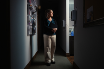 A photo of woman standing in shadowy hallway next to a patient exam room