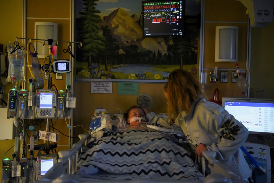 A woman comforts her young son who lies in a hospital bed on a ventilator.
