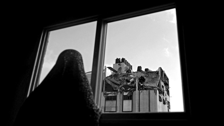 A woman looks through a window at the rooftop of a building which was hit by an airstrike.