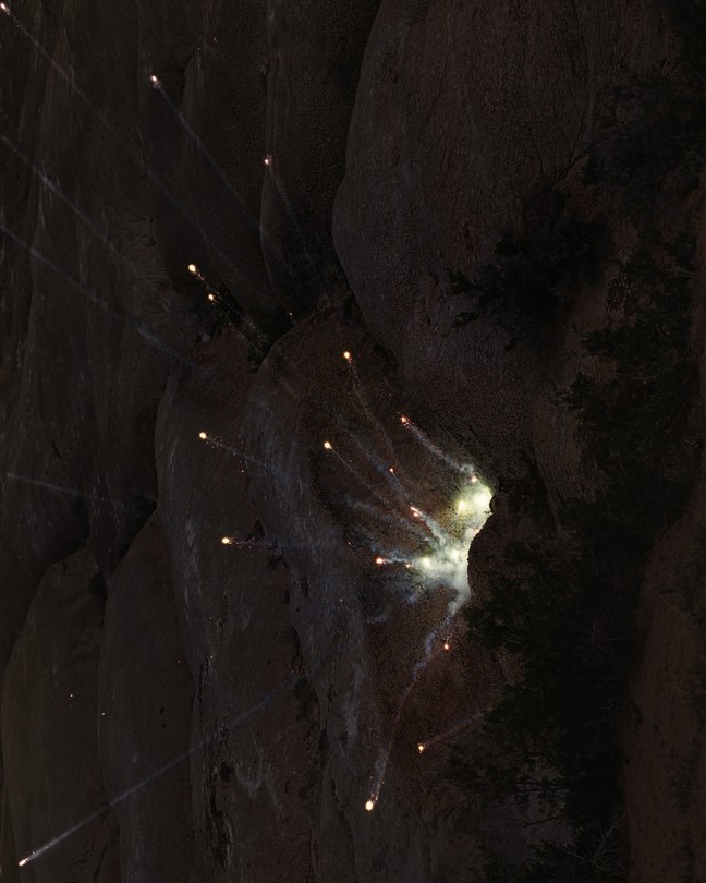 A firecracker hits a rock face at night.