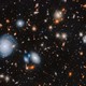 An image of many glowing galaxies in deep space, in various shapes and colours, on a black background