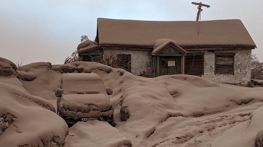 Thick gray ash blankets a house, a car, and the snow-covered ground.