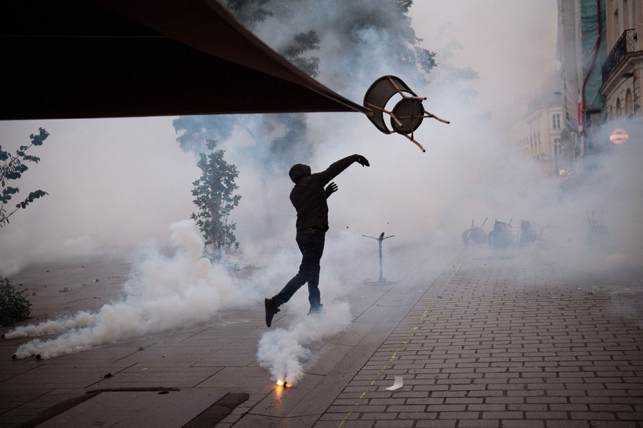 A protester throws a chair in a plaza amid smoke or tear gas.