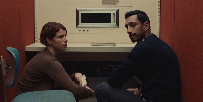 Jessie Buckley and Riz Ahmed sitting together in a retro room