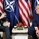 Photograph of Donald Trump in conversation with Mark Rutte, seated in front of U.S. and NATO flags.