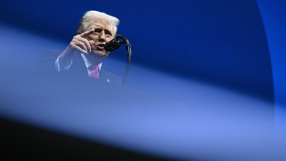 Donald Trump speaks into a microphone at a podium against a blue background.