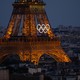 An elevated view of Paris buildings and part of the Eiffel Tower, with the Olympic rings mounted on the tower's side