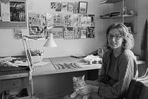 Black-and-white photo of artist Christina Ramberg seated in her studio with a cat in her lap.