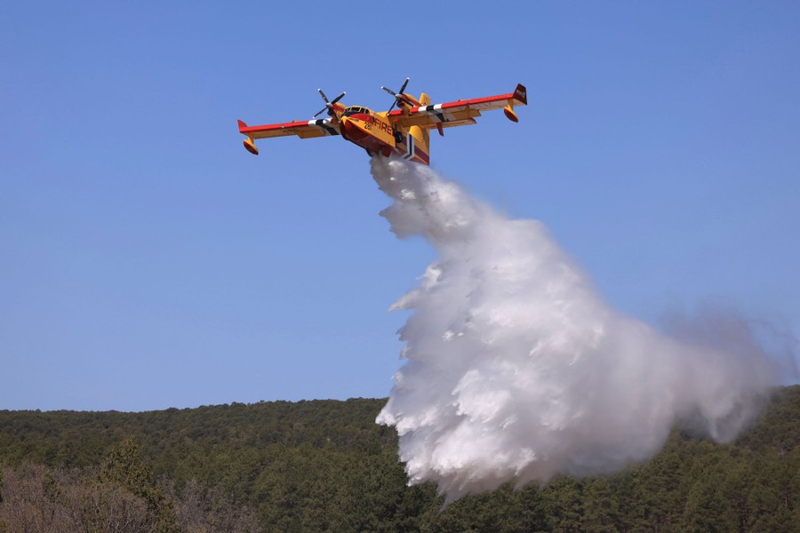 A firefighting airplane drops water onto a forest.