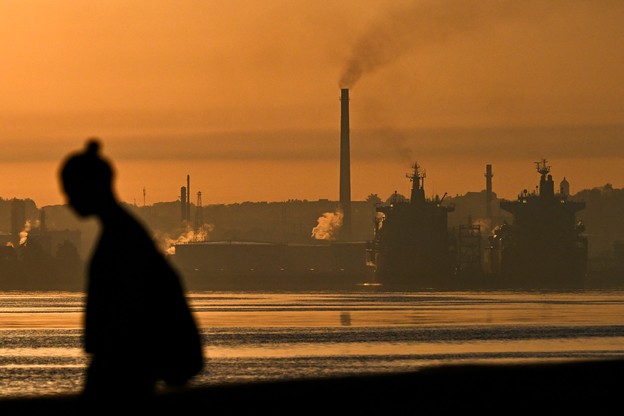 The silhouette of a person walks in front of a backdrop of an oil refinery in Havana, with an orange, smoky sky