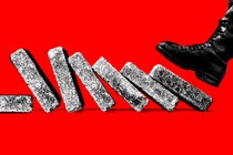 A foot in a military boot comes down on the first of a line of bricks set up like dominoes to topple