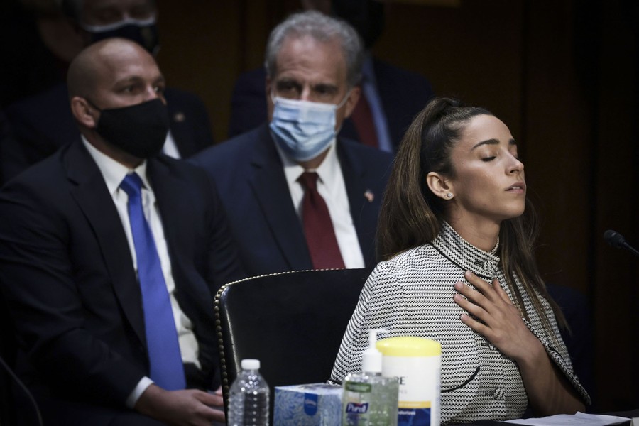 A woman sits before a desk, her eyes closed, her hand on her chest.