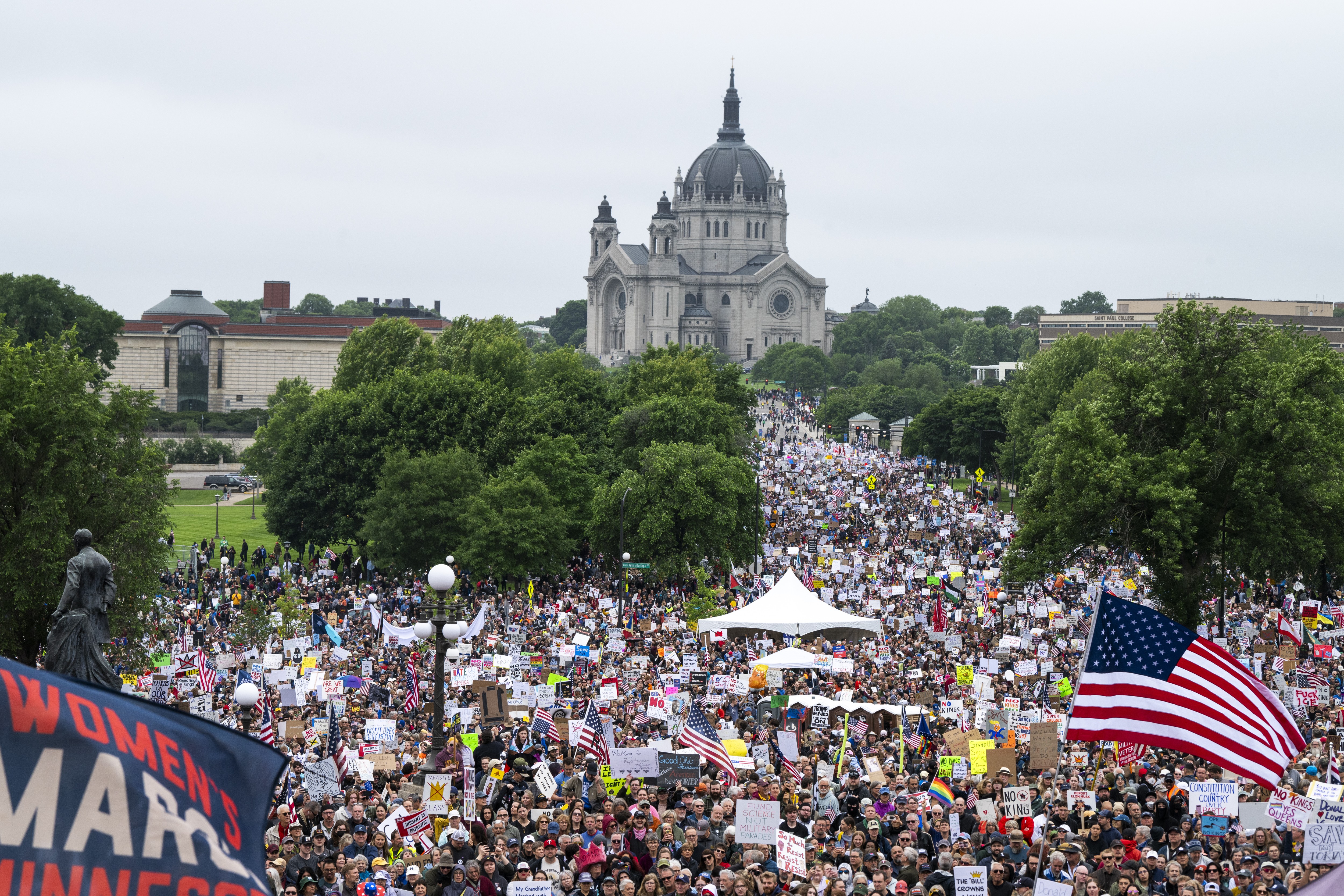 A large group of protesters marches on a street in front of a state capital building.