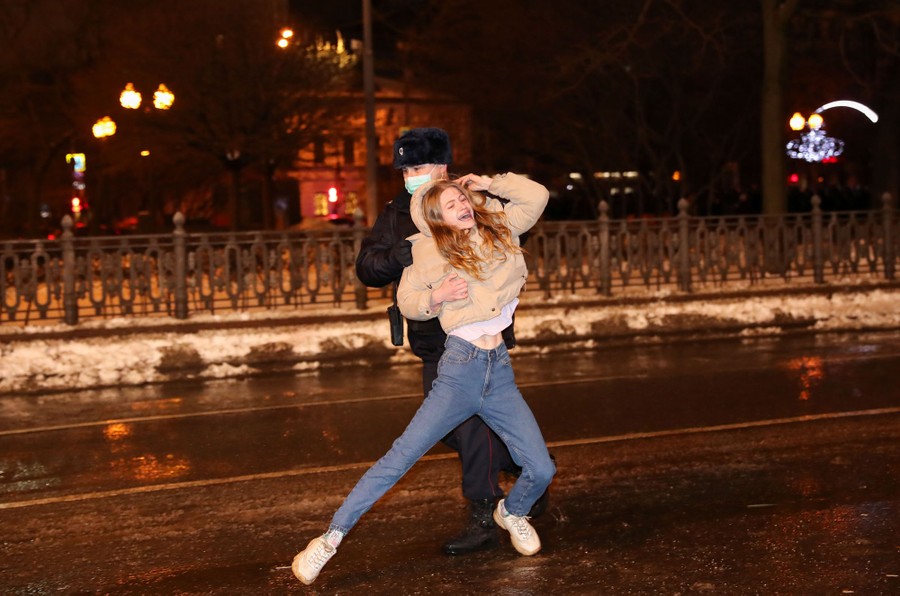 An officer pushes a woman along a street at night, as she struggles to resist.
