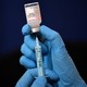 An image of a pair of gloved hands inserting a syringe into a vaccine vial