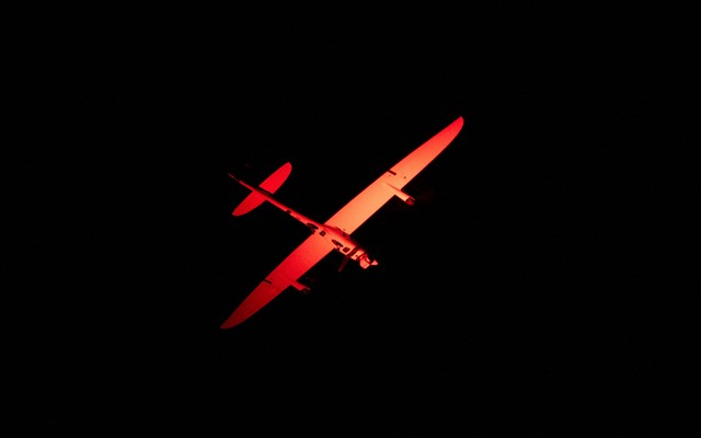 A plane in the pitch-black night sky is lit orange.