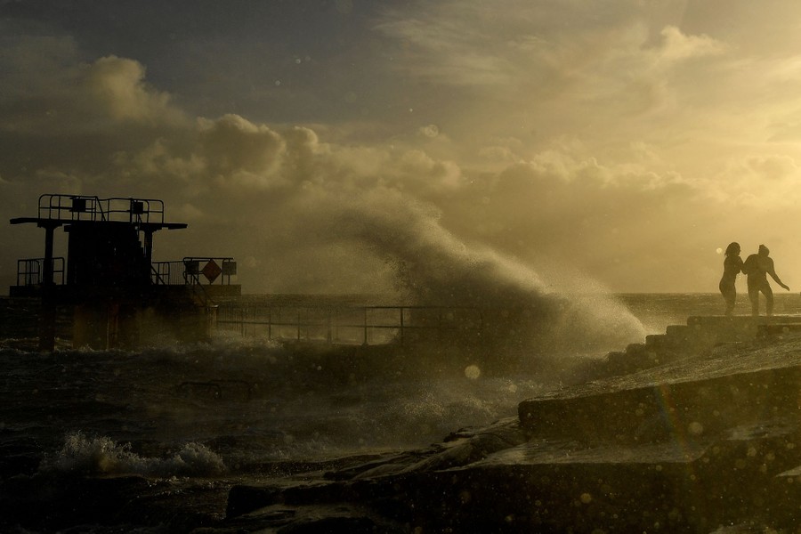People in bathing suits walk near a shoreline as winds drive large waves.