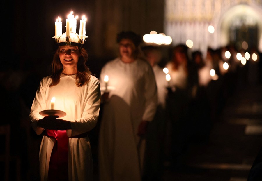 A person wears headgear covered in many lit candles while walking and singing inside a cathedral.