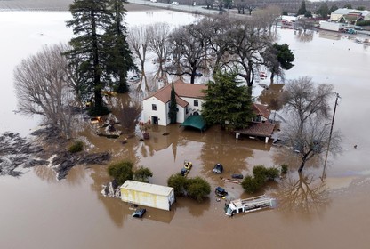 A two-story white house in California shown surrounded on all sides by muddy water halfway up its first level