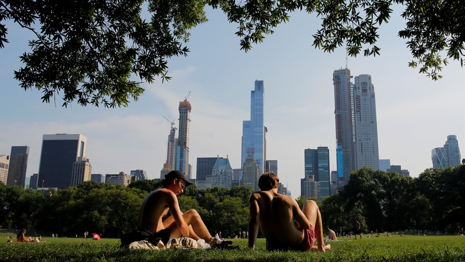Two male figures recline on a grassy field. Manhattan's skyscrapers rise in the background.