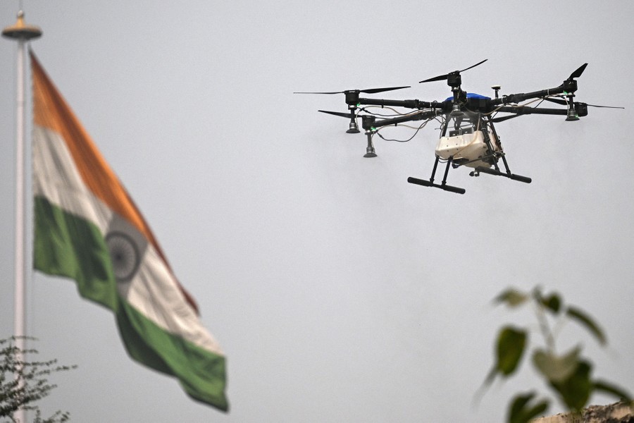A drone carrying a small tank of water flies near an Indian flag.