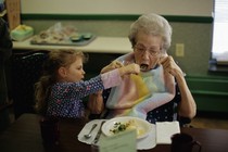 A toddler feeding an elderly woman from a fork.