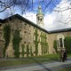 Two people walk past a brick, ivy-covered building on the Princeton University campus.