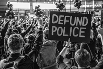 black-and-white photo of protest crowd with fists raised, with sign "DEFUND POLICE"