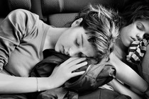 a black and white photo of two girls asleep while sitting, one leaning on the other