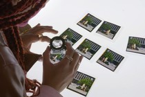 A woman uses a magnifying glass to look at thumbnails from Seeking Mavis Beacon