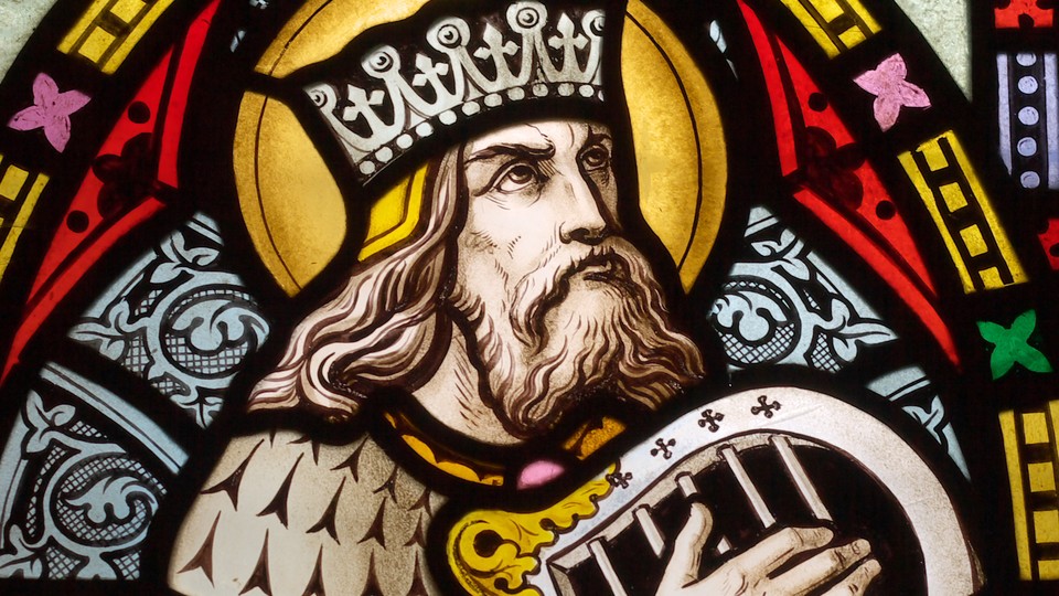 A stained-glass window of King David wearing a crown and playing a hand harp