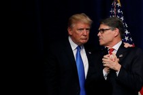 President Donald Trump huddles with Secretary of Energy Rick Perry in front of a curtain and an American flag.