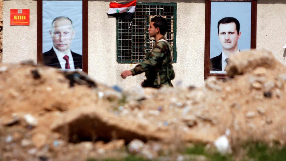 A Syrian government soldiers walks past rubble and posters of Bashar al-Assad and Vladimir Putin.