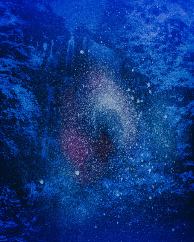 A blue-ish purple tinted print photograph by Prin Rodriguez of an explosion of starlight superimposed on a hazy landscape