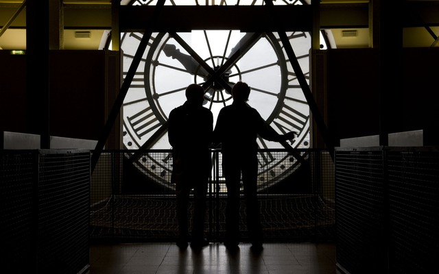 Two people are backlit while looking at a large clock