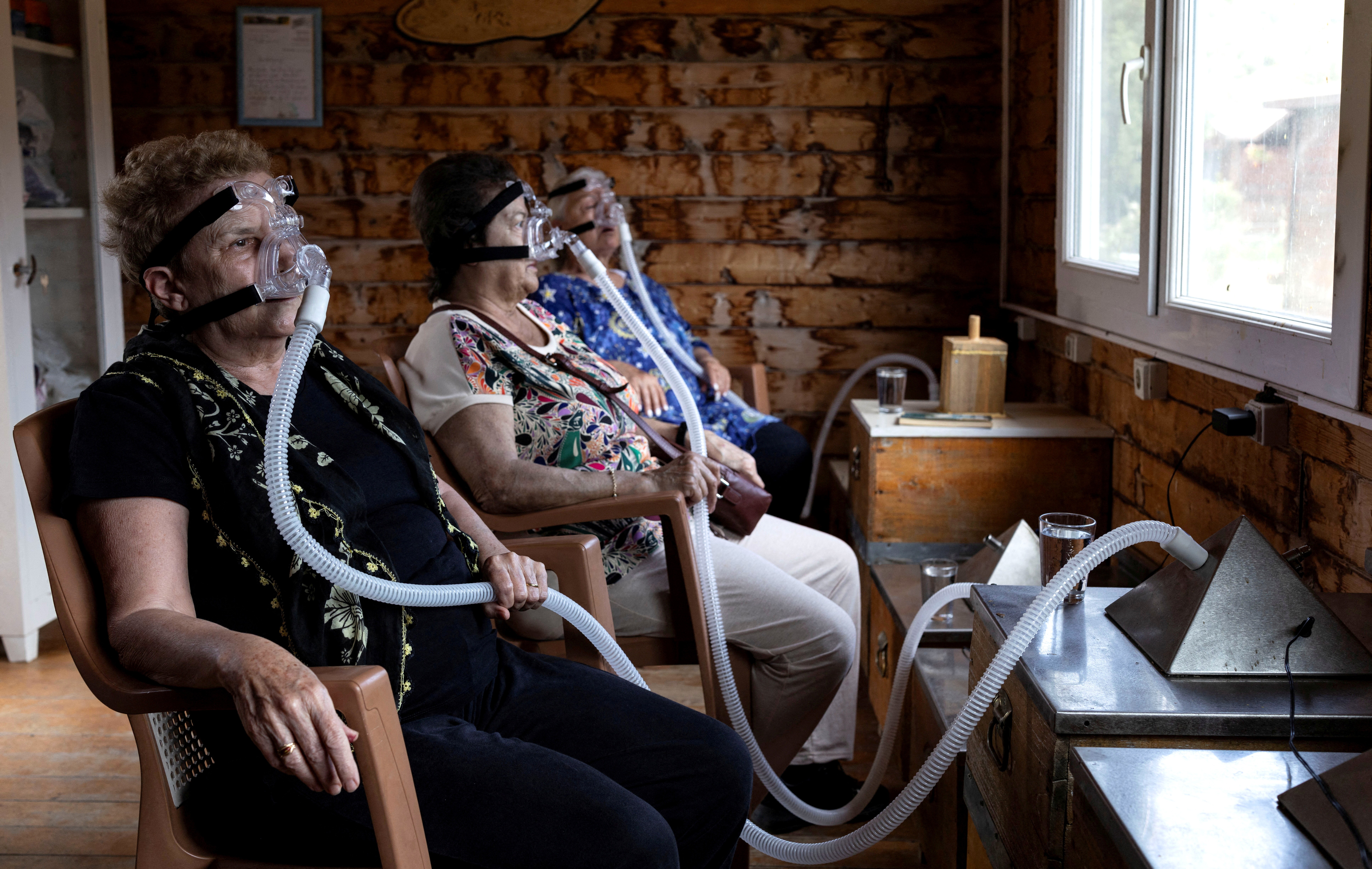 Three women sat in a chair, each wearing a ventilator mask, connected to long hoses that were obviously connected to beehives.