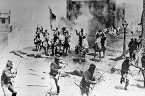 black-and-white film still from scene of street battle in town with armed Ku Klux riders firing against uniformed men with rifles