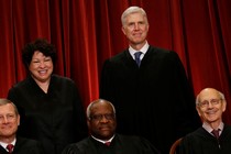 Supreme Court justices stand in front of a red backdrop. 