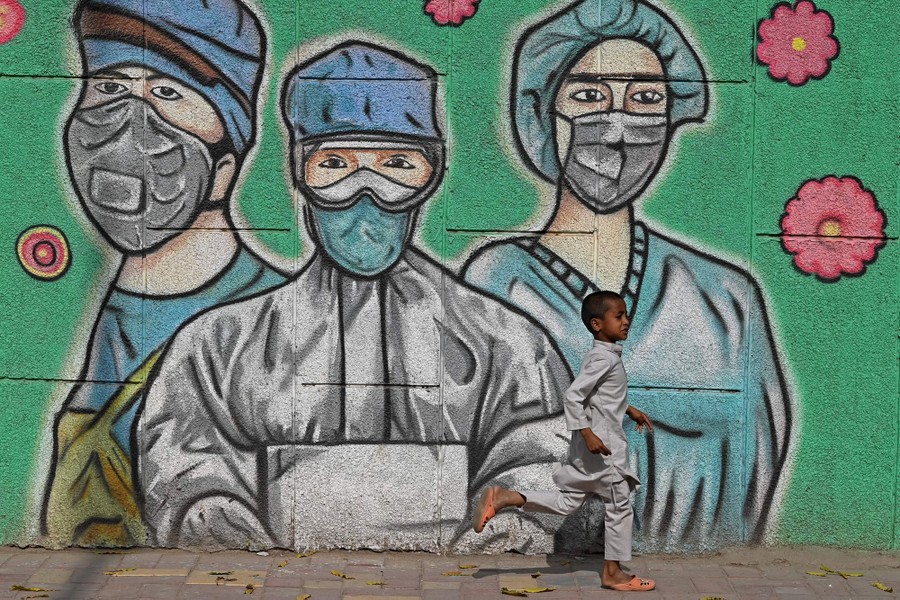 A child runs past a wall mural depicting frontline COVID-19 workers wearing face masks.