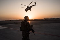 A soldier holding a gun in a helipad at sunset