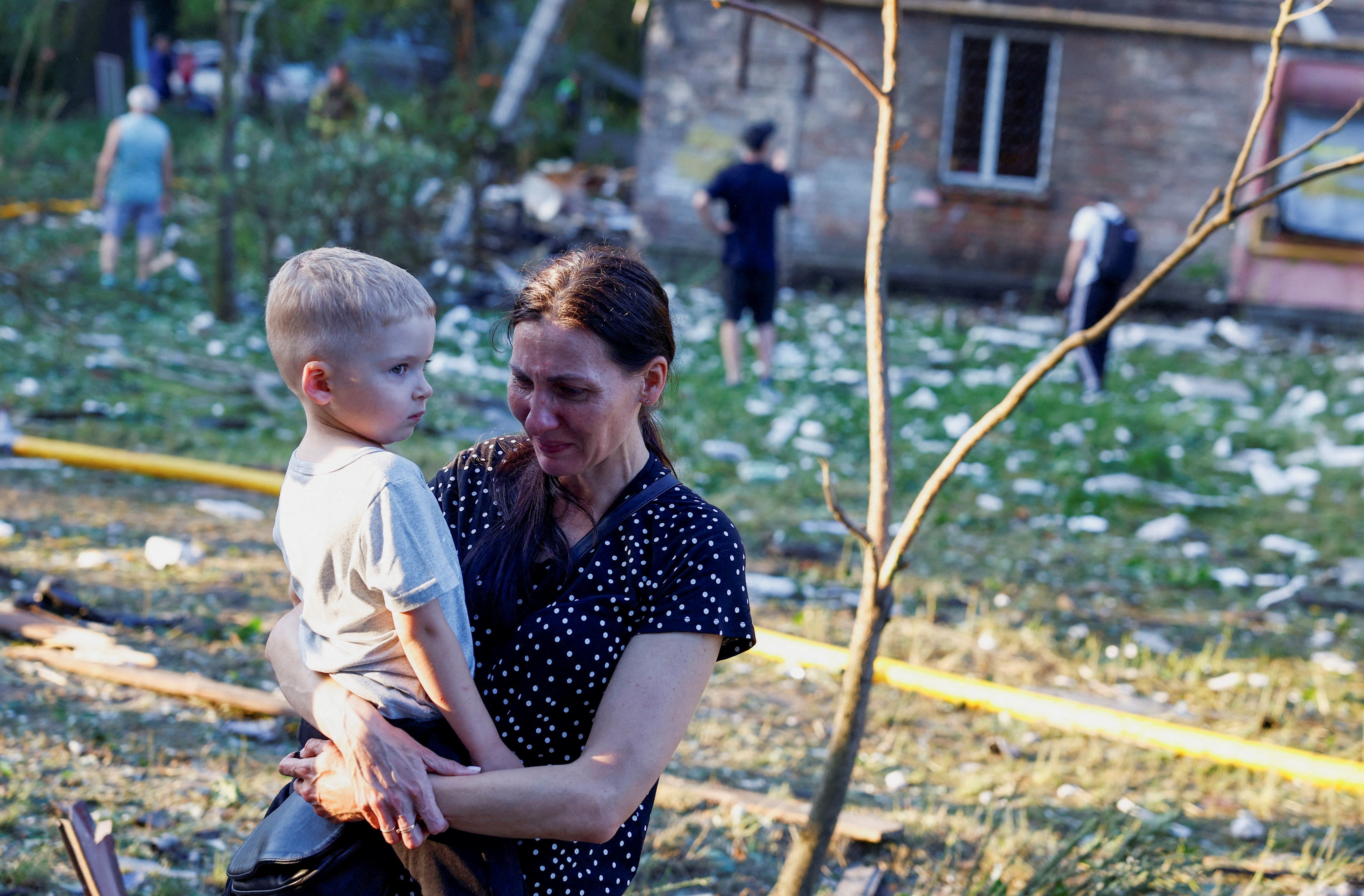 A woman cries while holding a child near a damaged apartment building.
