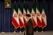 Khamenei, looking down, walks past a bank of seven Iranian flags with a portrait of Ayatollah Ruhollah Khomeini above them.