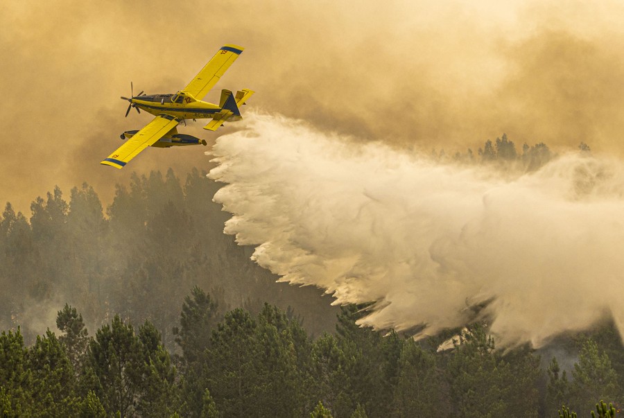 A small firefighting aircraft drops water onto a forest fire.