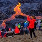 People gather on a hillside overlooking an active lava flow.