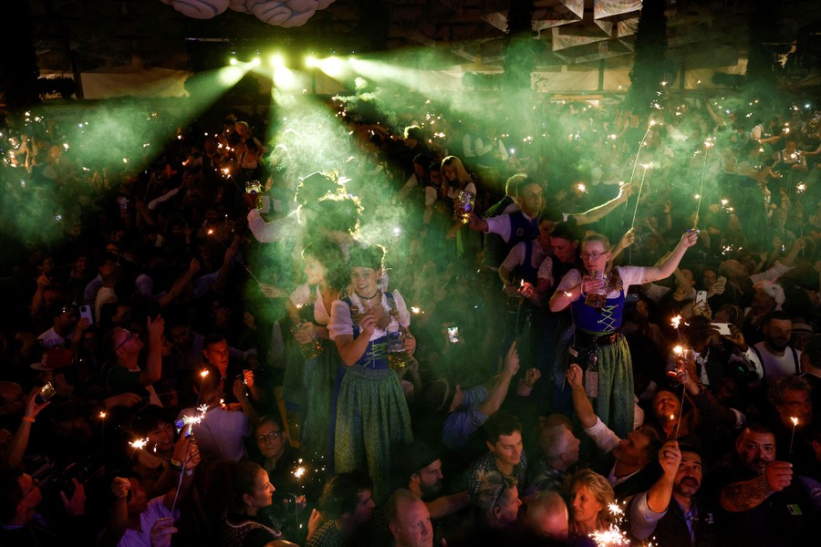 Waiters and customers in a beer hall celebrate while holding sparklers and glasses of beer.