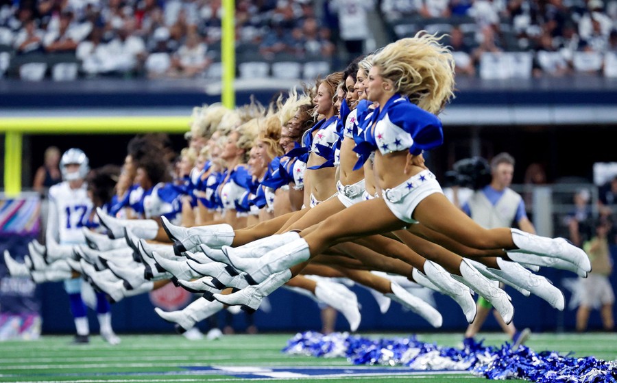 A line of NFL cheerleaders jump and kick their legs up at the same time.