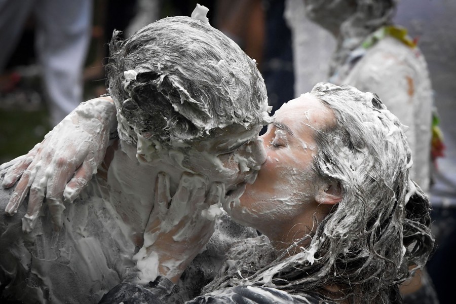 Two foam-covered students kiss, among others participating in a shaving foam fight.