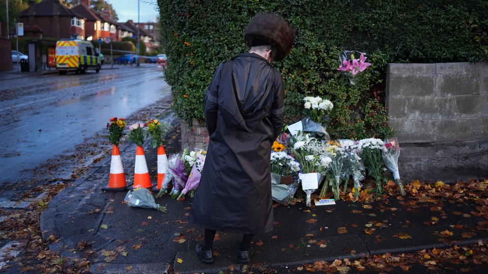 An Orthodox man pays respects at a street corner piled with bouquets of flowers.