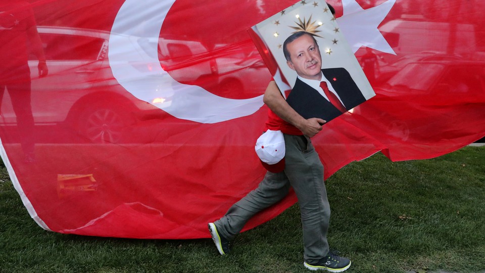 An Erdoğan supporter carries a poster with his face in front of a Turkish flag.