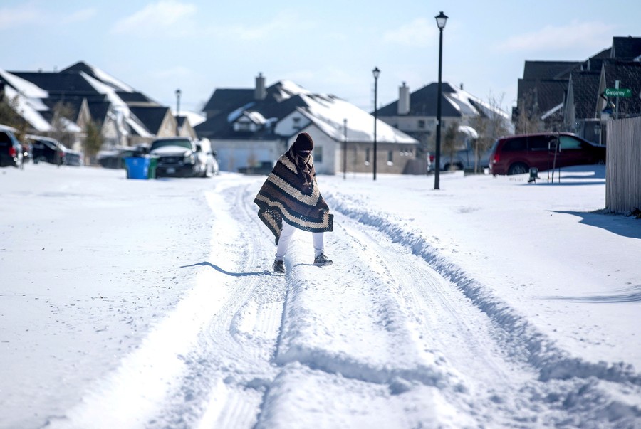 A person walks across a residential street that is covered in snow.